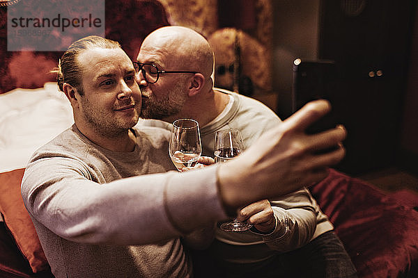 Mann  der seinen Freund küsst  während er im Hotelzimmer Wein genießt