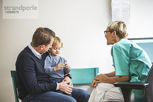 Seitenansicht einer reifen Ärztin  die mit einem Jungen spricht  dessen Vater in der Klinik ist