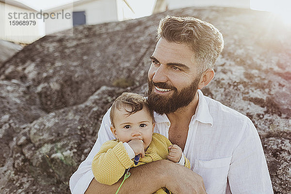 Porträt eines kleinen Mädchens mit dem Vater  der auf einer Felsformation sitzend wegschaut