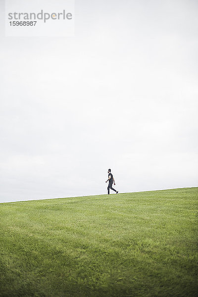 Seitenansicht eines jungen Mannes  der auf einem Grasfeld vor bewölktem Himmel geht