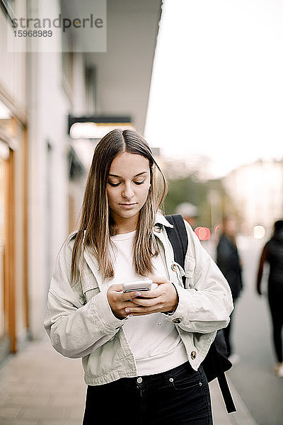 Teenager-Mädchen schreibt auf dem Fußweg in der Stadt per Handy SMS