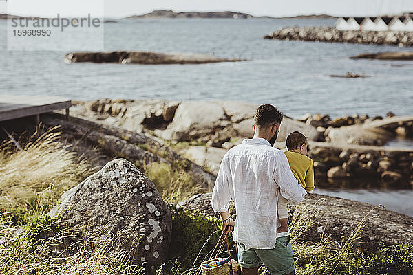 Rückansicht eines Vaters mit Tochter beim Spaziergang auf einer Felsformation am Meer