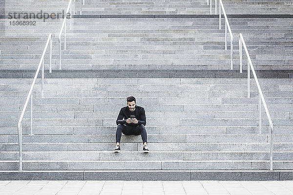 Junger Mann benutzt Mobiltelefon  während er auf einer Treppe sitzt