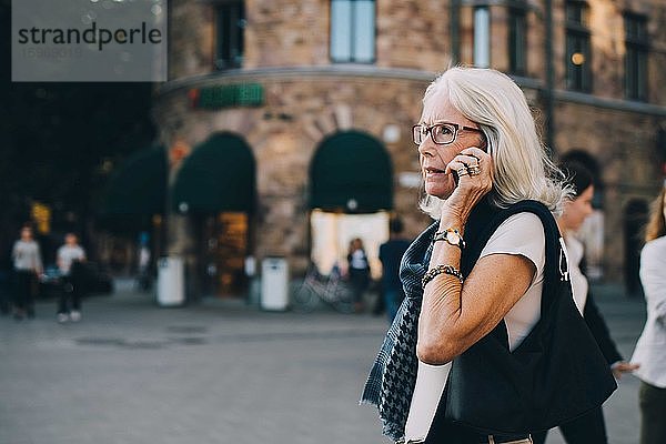 Ältere Frau spricht durch ein Smartphone  während sie in der Stadt wegschaut