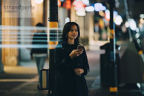 Junge Frau schaut weg  während sie nachts in der Stadt mobil telefoniert