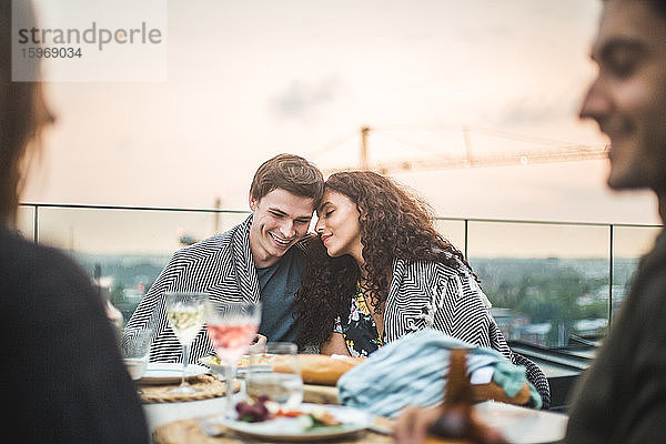 Lächelnder Mann und lächelnde Frau sitzen bei Sonnenuntergang mit Decke auf der Terrasse
