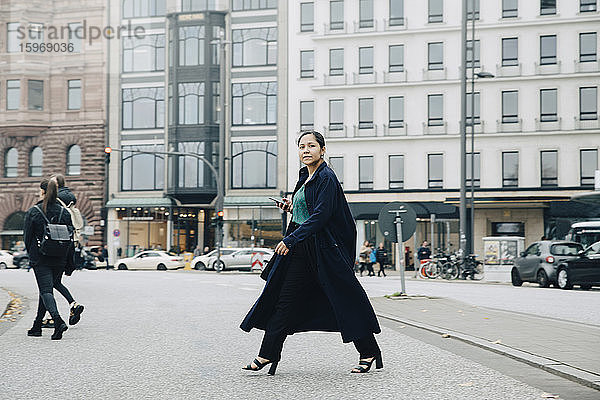 Porträt einer Unternehmerin in Jacke beim Überqueren der Straße in der Stadt