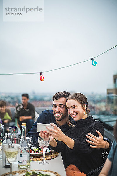 Fröhliche Freunde mit Getränken  die sich während der Dachfeier per Smartphone selbstständig machen