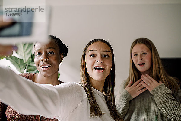 Lächelnde Mädchen im Teenageralter  die sich zu Hause mit dem Handy selbstständig machen