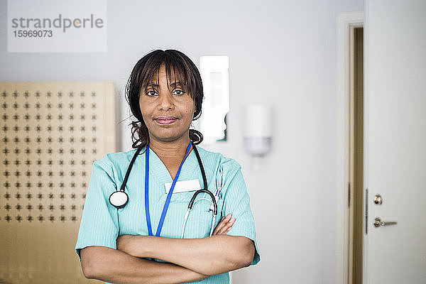 Porträt einer reifen Gesundheitshelferin mit verschränkten Armen stehend in der Klinik