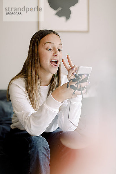 Teenagermädchen  die zu Hause sitzend Selbsthilfe per Mobiltelefon nimmt