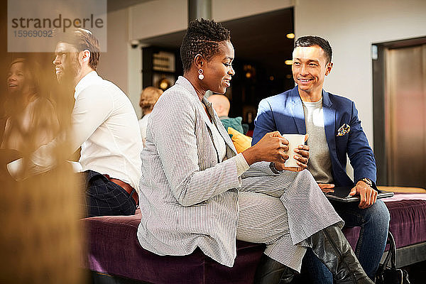 Lächelnde weibliche und männliche Geschäftsleute kommunizieren  während sie im Büroseminar sitzen
