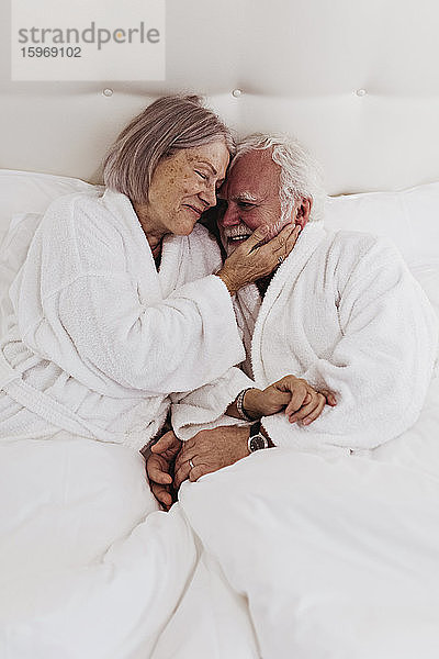 Lächelndes romantisches Seniorenpaar auf dem Bett im Hotelzimmer
