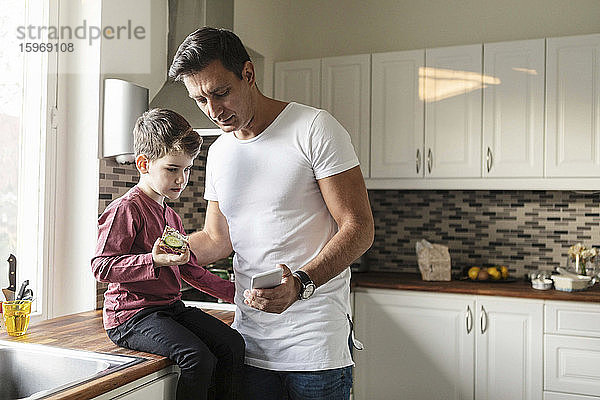 Vater zeigt dem Sohn ein Smartphone mit Essen  während er an der Küchentheke steht