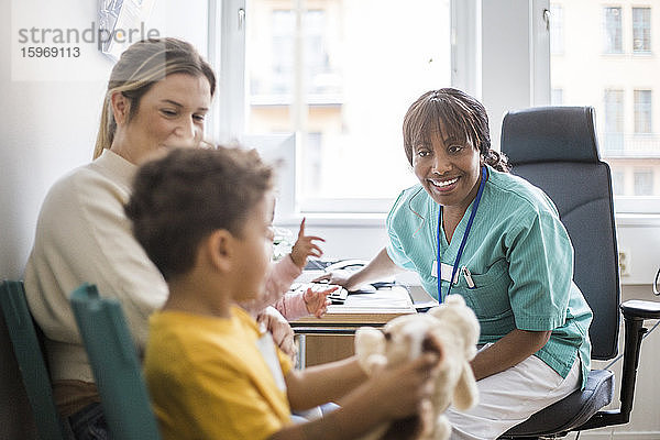 Lächelnder Kinderarzt spricht mit dem Jungen  während die Mutter in der Klinik sitzt