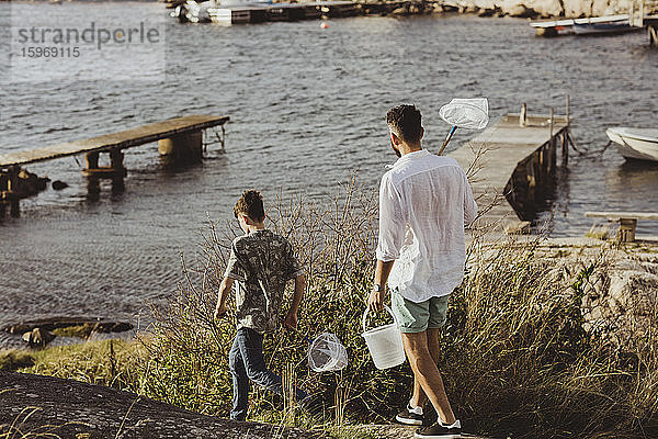 Rückansicht von Vater und Sohn  die am Wochenende mit einem Fischernetz auf dem Meer spazieren