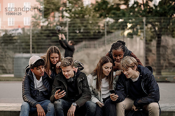 Multiethnische Teenager-Freunde benutzen Smartphones  während sie in der Stadt im Park sitzen