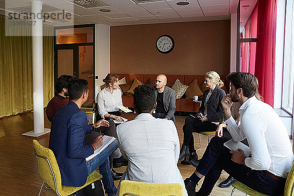 Unternehmer und Unternehmerinnen diskutieren im Kreis sitzend während eines Büro-Workshops