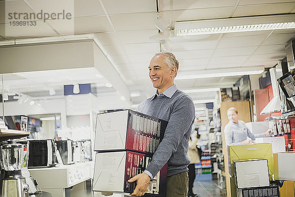 Lächelnder reifer Verkäufer mit Kisten im Elektronikladen