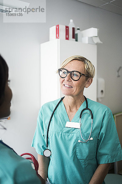 Lächelnder reifer Kinderarzt im Gespräch mit weiblichem Pflegepersonal in der Klinik