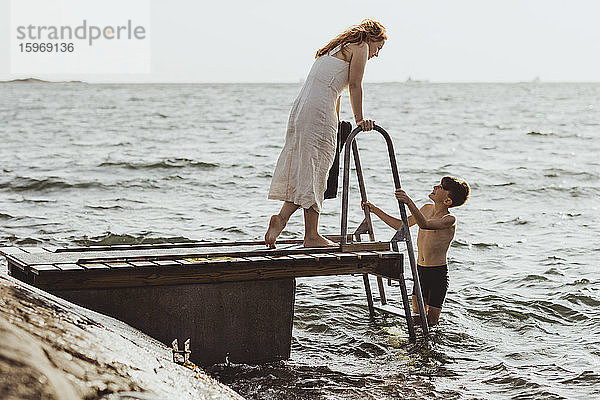 Seitenansicht einer Frau  die spricht  während ihr Sohn auf einer Leiter im Meer steht
