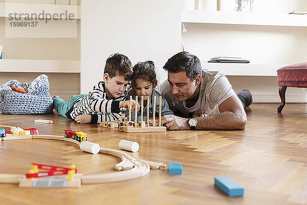 Kinder spielen mit dem Spielzeugblock  während sie mit dem Vater auf dem Hartholzboden liegen