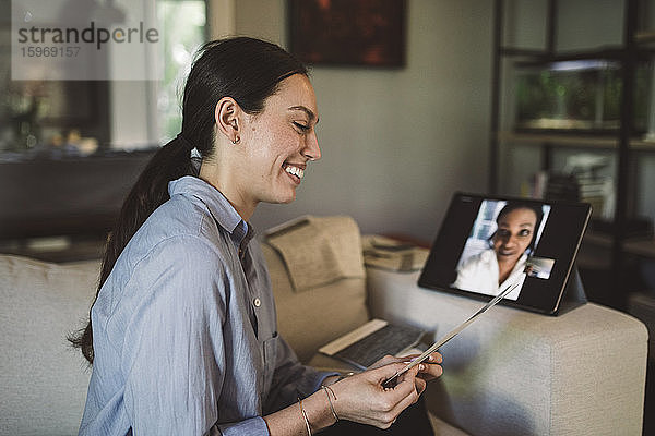 Lächelnde Unternehmerin mit Stoffmuster spricht per Laptop per Videokonferenz bei der Arbeit zu Hause