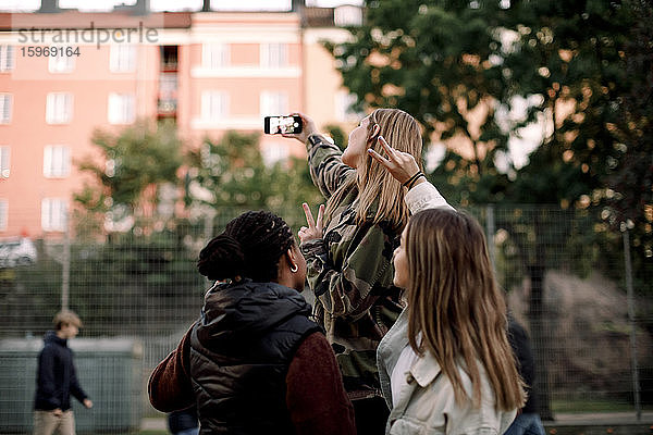 Teenager-Mädchen zeigen Friedenszeichen  während sie sich in der Stadt per Handy selbstständig machen