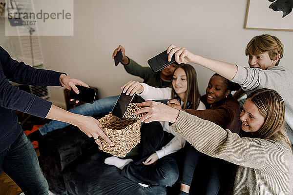 Mädchen und Jungen im Teenageralter halten Mobiltelefone im Korb zu Hause