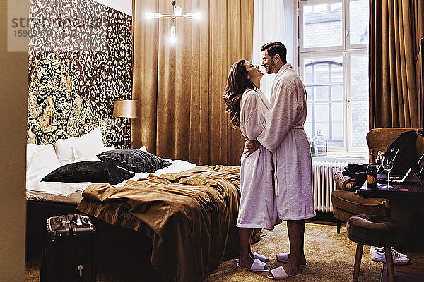 Seitenansicht eines romantischen Paares  das sich umarmt  während es im Hotelzimmer am Bett steht