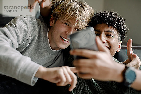 Lächelnde Teenager  die sich zu Hause mit einem Smartphone selbstständig machen