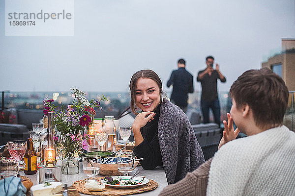 Lächelnde Freundinnen unterhalten sich bei geselligem Beisammensein auf der Terrasse