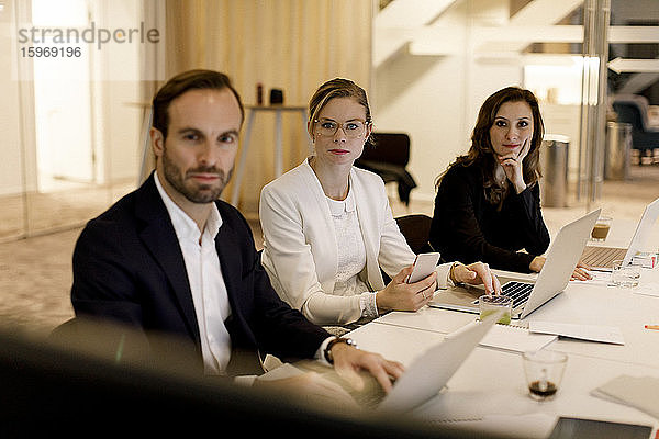 Männliche und weibliche Berufstätige im mittleren Erwachsenenalter  die bei Besprechungen zuhören  während sie im Büro am Konferenztisch sitzen