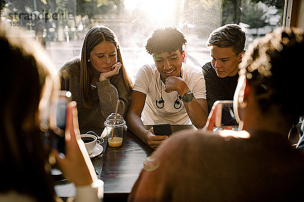 Mädchen und Jungen im Teenageralter nutzen soziale Medien auf Smartphones  während sie im Café sitzen