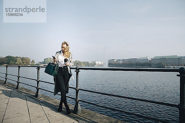 Unternehmer in voller Länge  der ein Mobiltelefon benutzt  während er in der Stadt am Meer steht