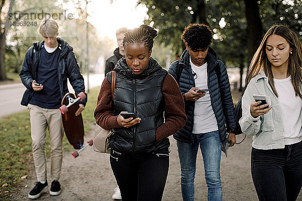 Multiethnische Freunde im Teenageralter benutzen Smartphones beim Gehen auf der Straße in der Stadt