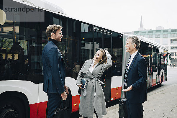 Lächelnde Geschäftsfrau mit männlichen Mitarbeitern steht in der Stadt gegen Bus