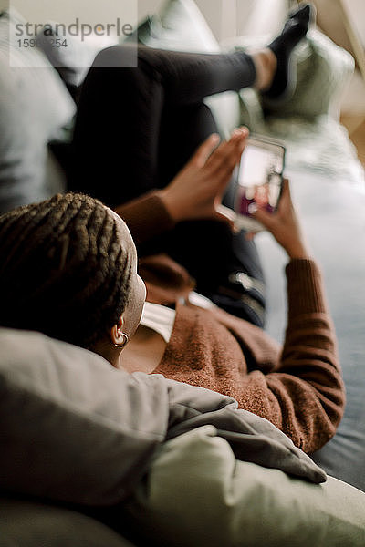 Teenager-Mädchen in voller Länge benutzt Smartphone  während sie zu Hause auf dem Sofa liegt