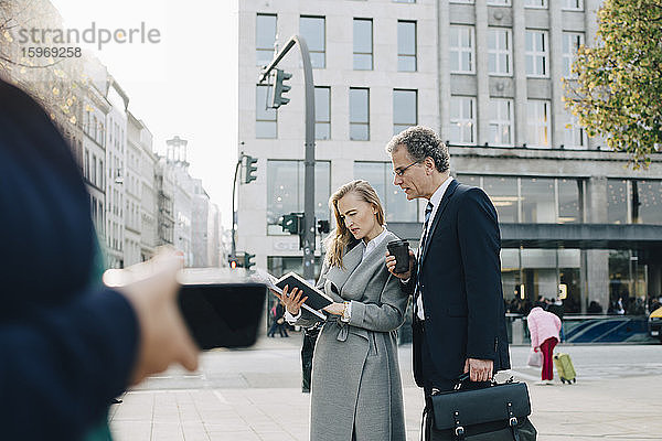Geschäftskollegen schauen im Buch  während sie in der Stadt stehen