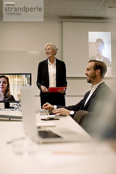 Lächelnder reifer Fachmann diskutiert mit Kollegen in Videokonferenz im Sitzungssaal