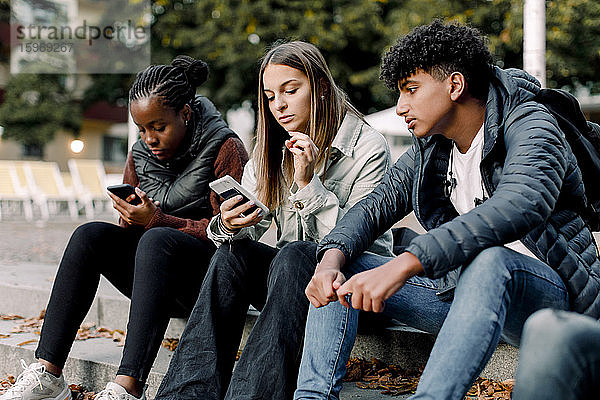 Teenager-Mädchen benutzen ein Smartphone  während sie mit einem Freund auf einer Treppe in der Stadt sitzen