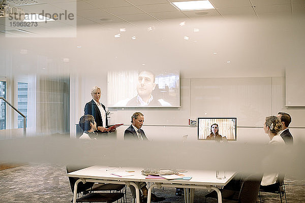 Männliche und weibliche Führungskräfte diskutieren in einer Webkonferenz mit Blick durch Glas am Arbeitsplatz