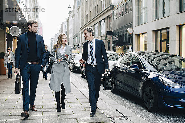 Geschäftsfrau mit männlichen Kollegen gehen in der Stadt auf dem Bürgersteig
