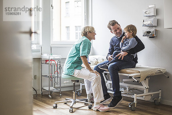 Seitenansicht einer lächelnden Ärztin  die mit einem Jungen spricht  dessen Vater in der Klinik ist