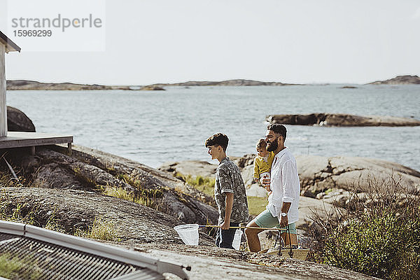 Seitenansicht eines Vaters mit Kindern  die an einem sonnigen Tag auf einer Felsformation laufen