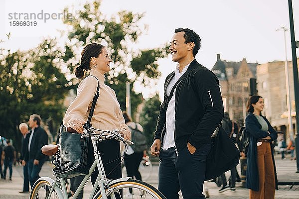 Lächelnde Frau mit Fahrrad  die einen männlichen Freund ansieht  während sie in der Stadt steht