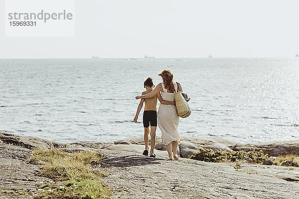 Rückansicht einer Frau mit Sohn  die an einem sonnigen Tag gegen das Meer läuft