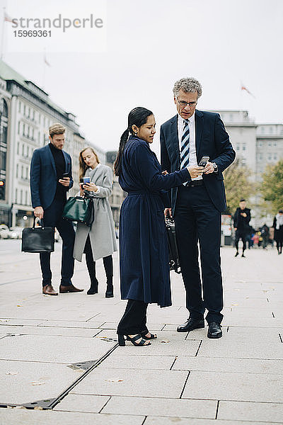 Unternehmerinnen und Unternehmer  die ein Smartphone benutzen  während sie in der Stadt auf der Straße stehen
