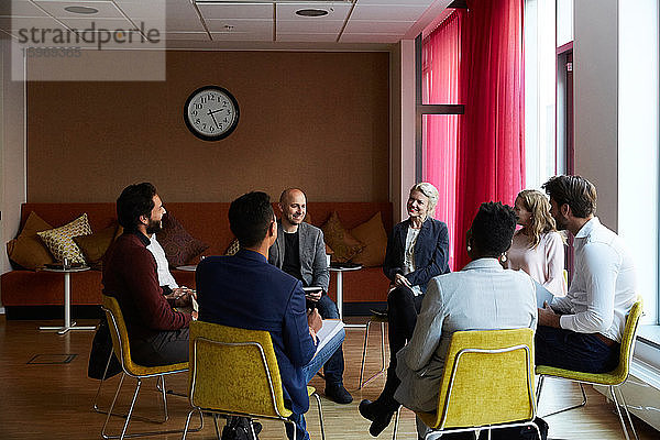 Lächelnde Unternehmer und Unternehmerinnen sitzen während des Büro-Workshops im Kreis