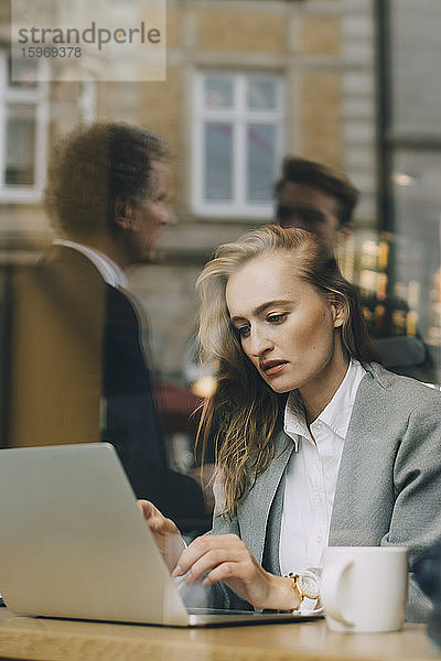 Geschäftsfrau arbeitet am Laptop im Café durch ein Glasfenster gesehen